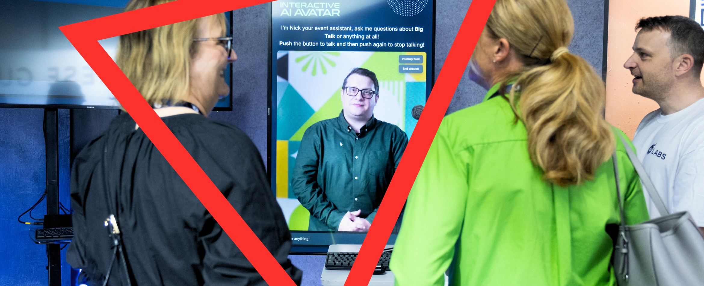 Three people at a conference or trade show event are engaging with an 'Interactive AI Avatar' display. The screen shows a man named Nick in glasses and a dark green shirt, who serves as an event assistant for answering questions about 'Big Talk.' Instructions on the screen read 'Push the button to talk and then push again to stop talking!' Three attendees - a woman in black, a woman in a bright green jacket, and a man in a white shirt - are gathered around the interactive display, which appears to be set up on a laptop with geometric yellow accent graphics framing the scene.