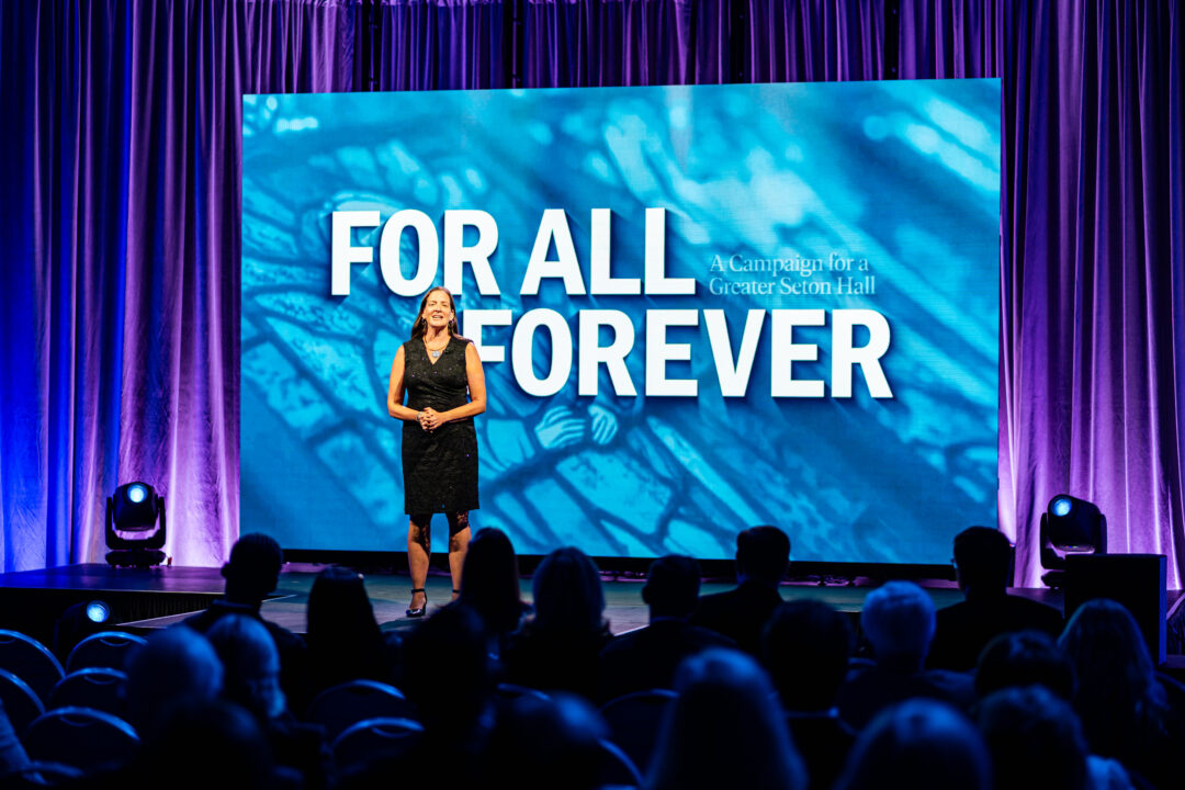 A woman standing on stage speaking to an audience.