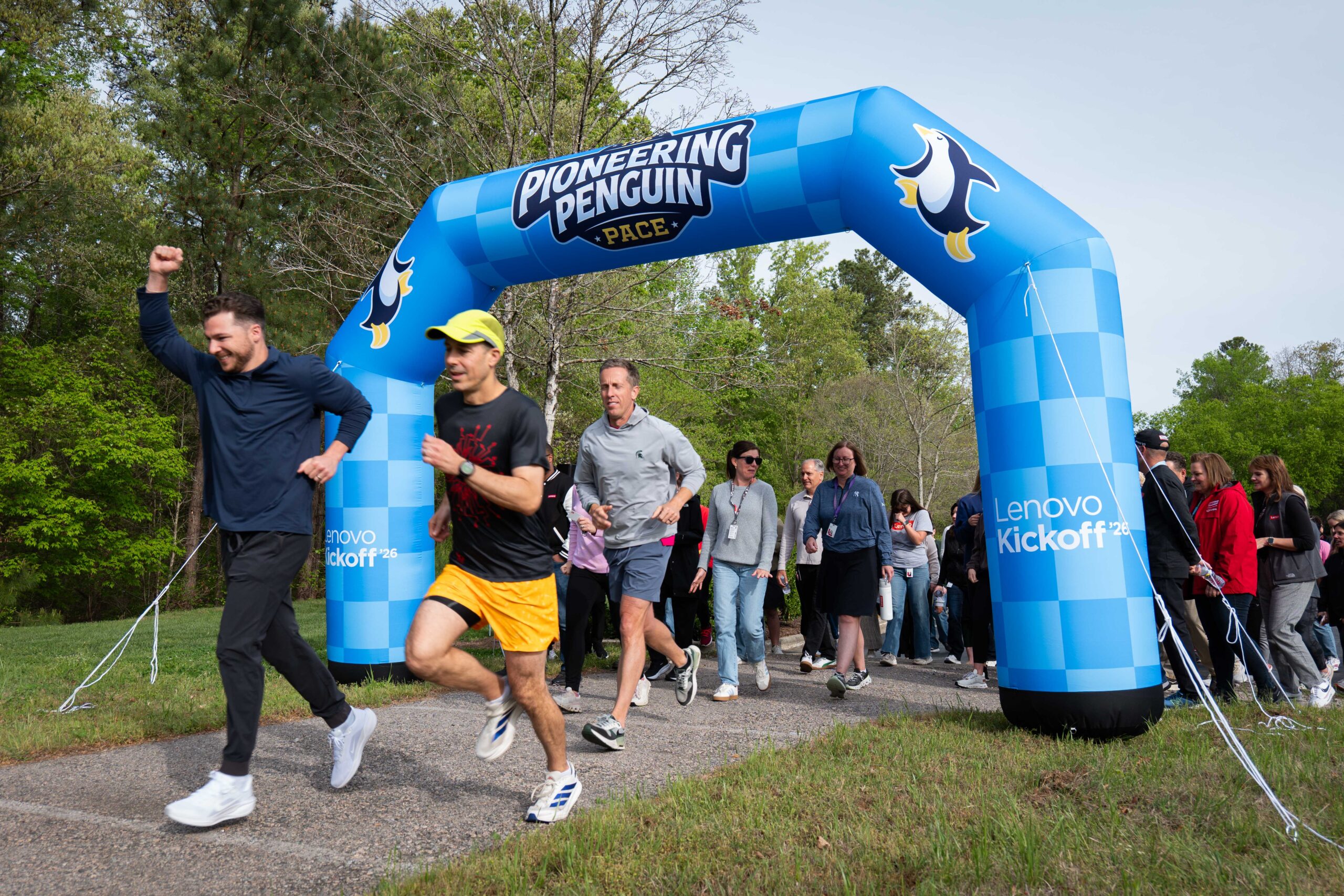 Lenovo Kickoff '26 attendees crossing the start/finish arch of the Pioneering Penguin Pace campus walk and run, a wellness activity held as part of the event program.