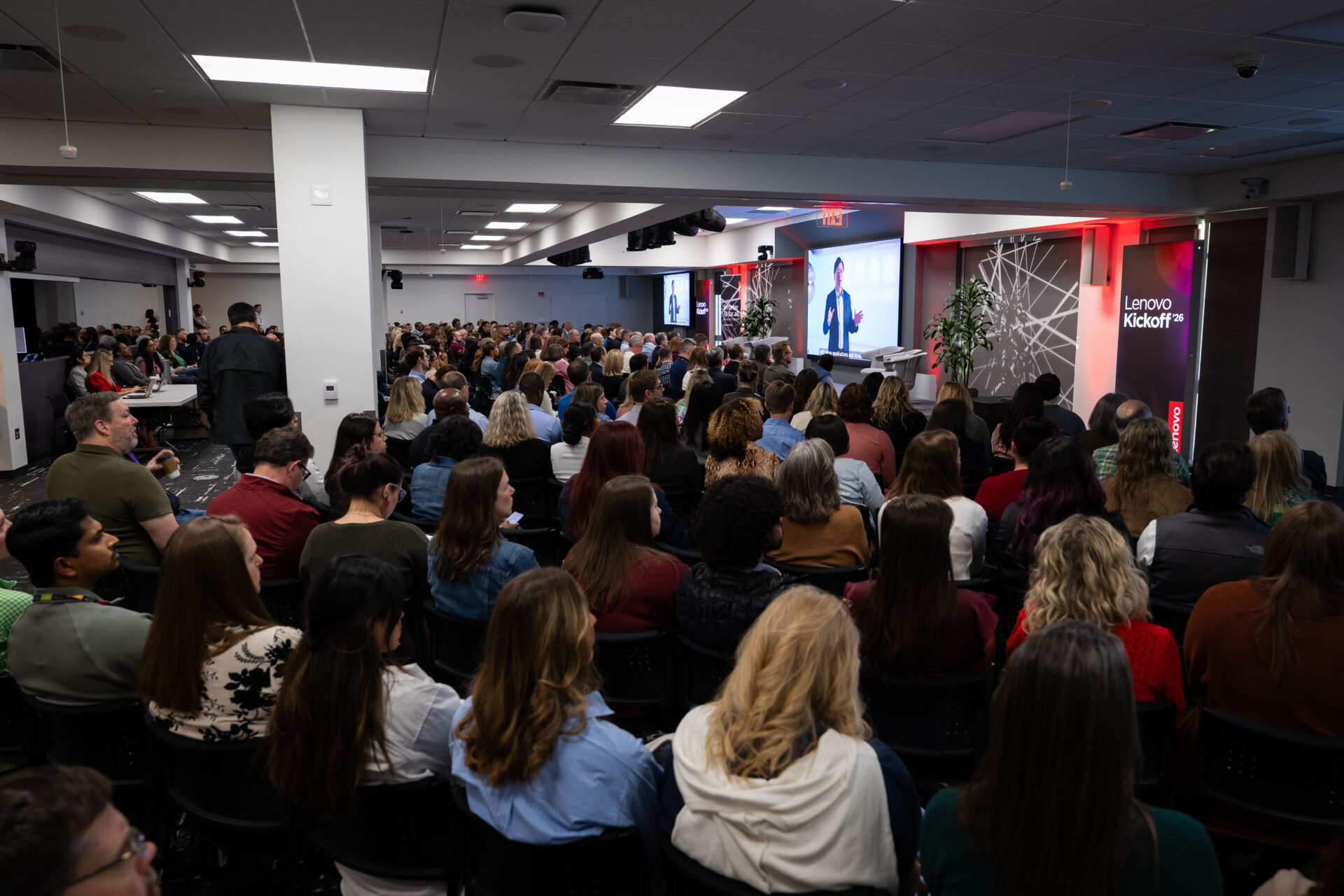 A capacity crowd of Lenovo employees watches the General Session broadcast at a Lenovo Kickoff '26 regional watch party, with branded signage and projection screens displaying the live stream.